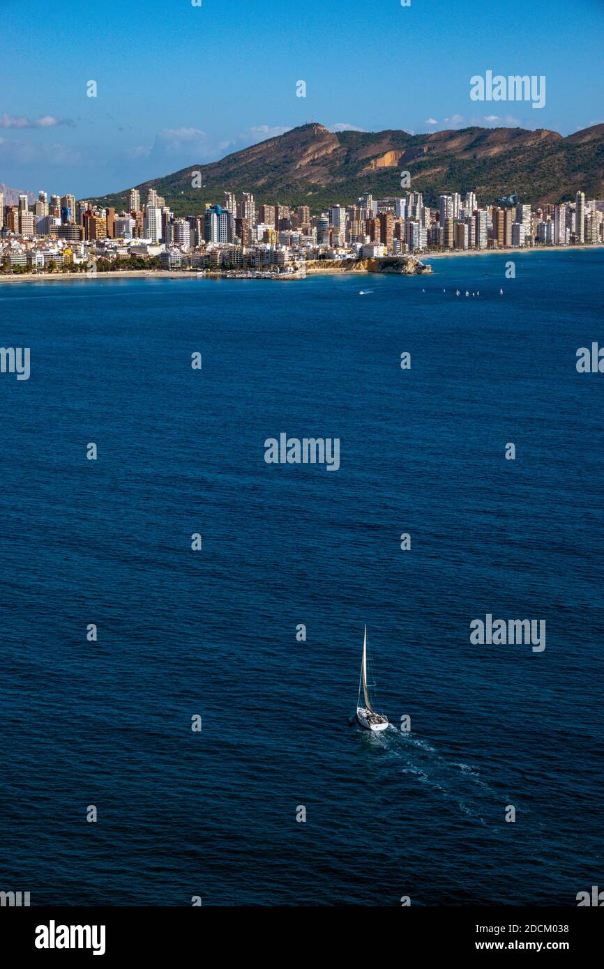 Piccolo yacht che naviga verso la popolare destinazione di vacanza e luogo di sole invernale di Benidorm, Costa Blanca, Spagna, visto dalla collina di Tossal de la Cala Foto Stock