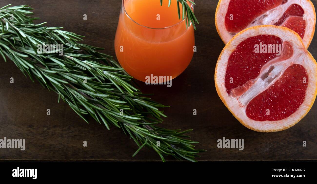 Due metà di arancio rosso, rametto di rosmarino e bicchiere di succo d'arancia giacenti su un tavolo di legno su sfondo chiaro Foto Stock