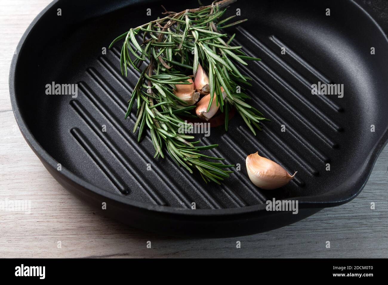 Padella nera su tavola di legno con rametti di rosmarino e spicchi d'aglio all'interno Foto Stock