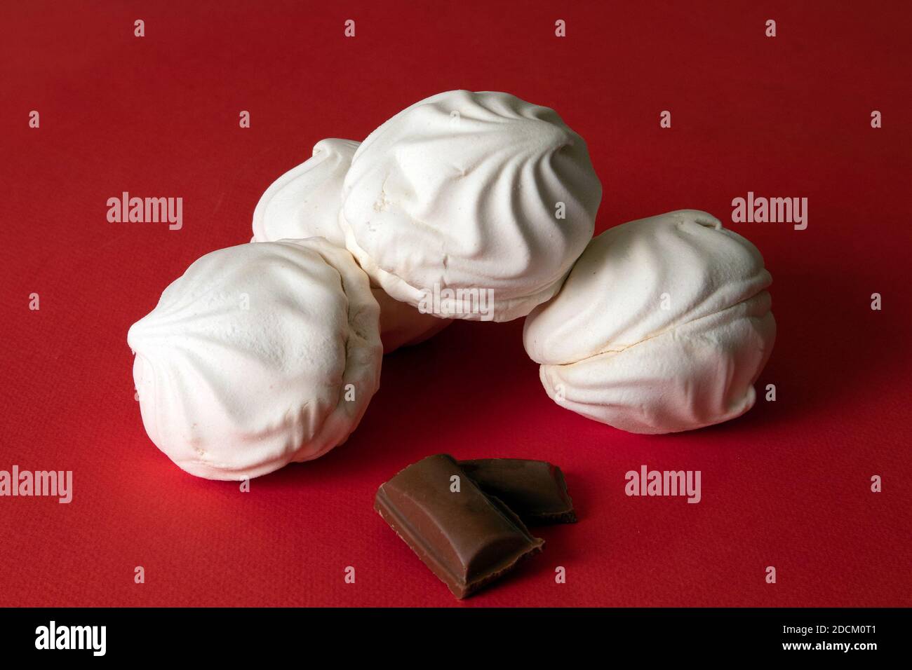Quattro zepiri bianchi delicati e piccoli pezzi di cioccolato contro sfondo saturo di colore rosso brillante Foto Stock