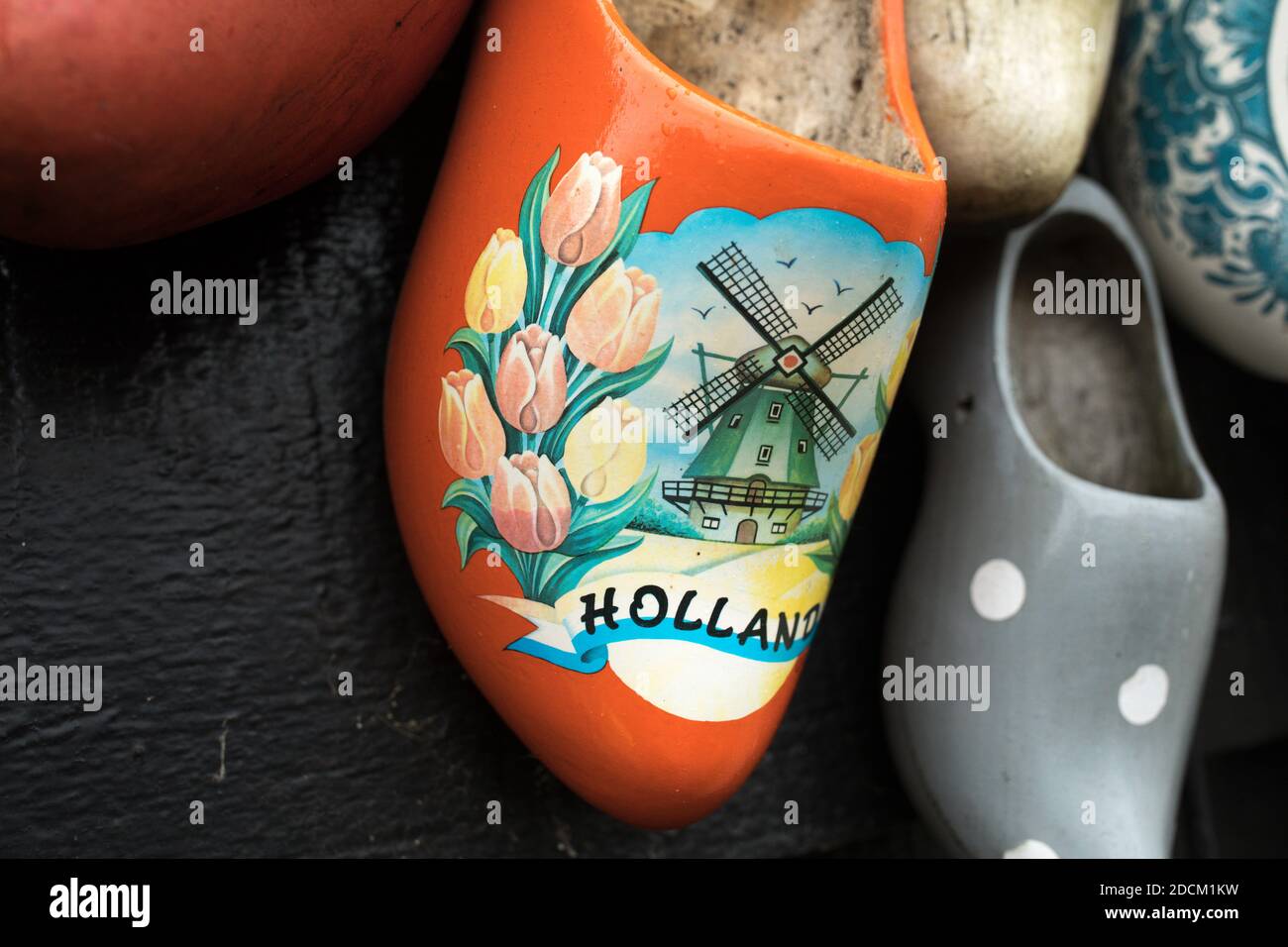 Scarpe di legno inchiodate su una porta nera di un vecchio fienile in Olanda. La scarpa di legno centrale è arancione con un mulino a vento olandese, un segno olandese e tulipani. Foto Stock