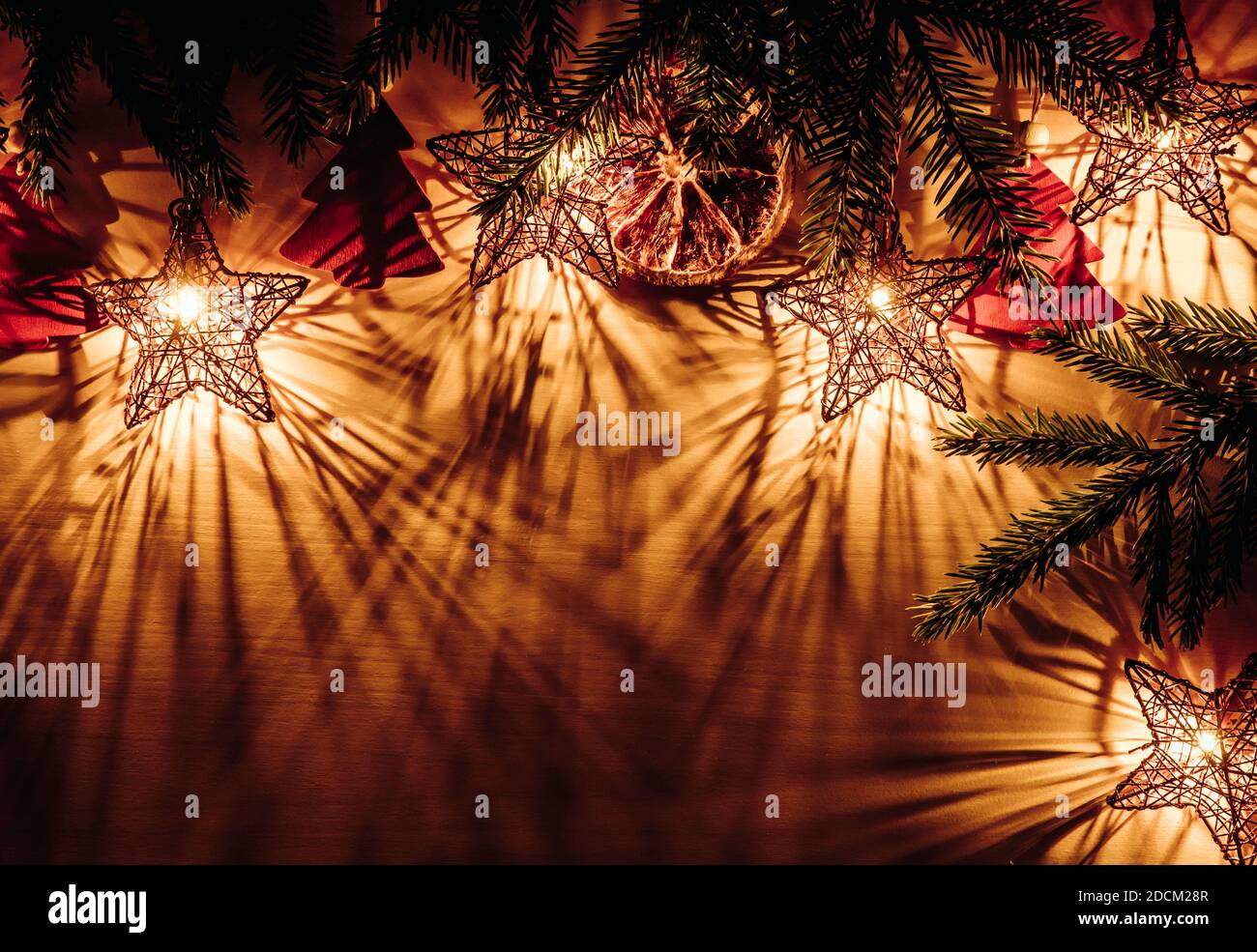 Sfondo di Natale, bordo superiore con rami di abete rosso forma stella luci partito illuminato, a fette arancio secco e figurine a forma di albero rosso. Foto Stock