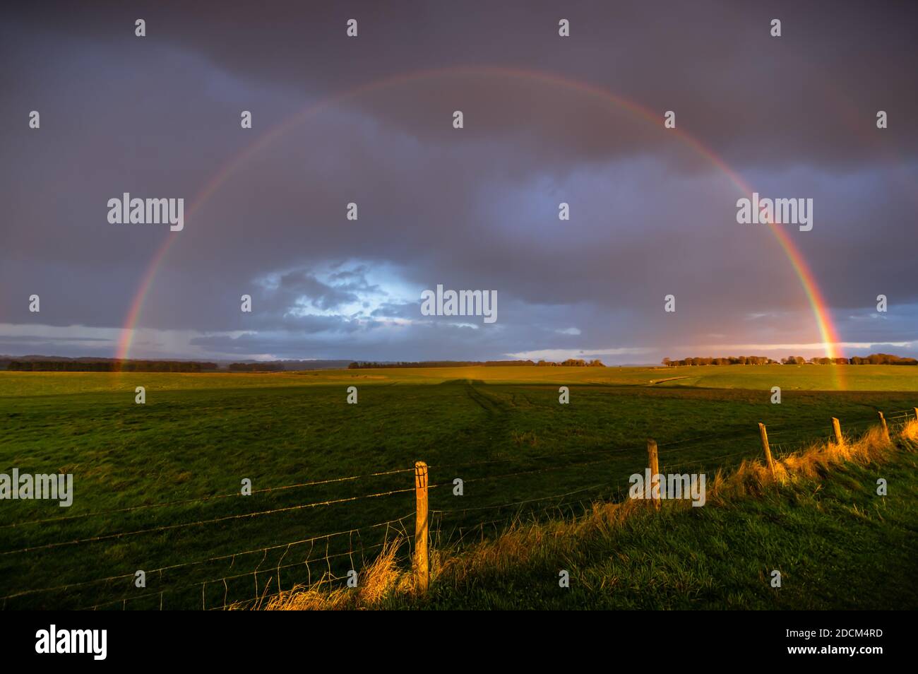 Una doccia a pioggia e una forte luce dorata al tramonto si combinano per formare un arcobaleno (con una debole banda doppia) nel sito di campagna di Stonehenge, Regno Unito. Foto Stock