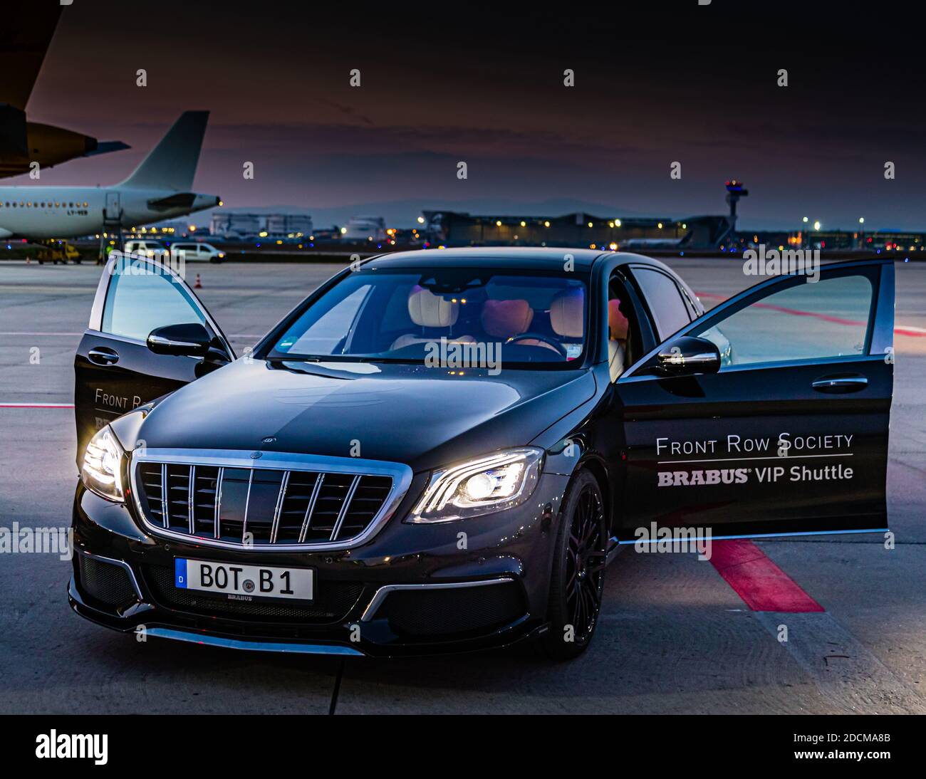 La porta di una Brabus Maybach S 900 reca la scritta "Brabus VIP Shuttle – VIP-Services" all'aeroporto di Francoforte, in Germania. Le segnaletiche stradali e le persone in giubbotti ad alta visibilità si riflettono nella vernice lucida. L'auto appartiene alla flotta di navette della festa "World Club Dome – Zero Gravity, The Platinum Edition" di BigCityBeats. Foto Stock