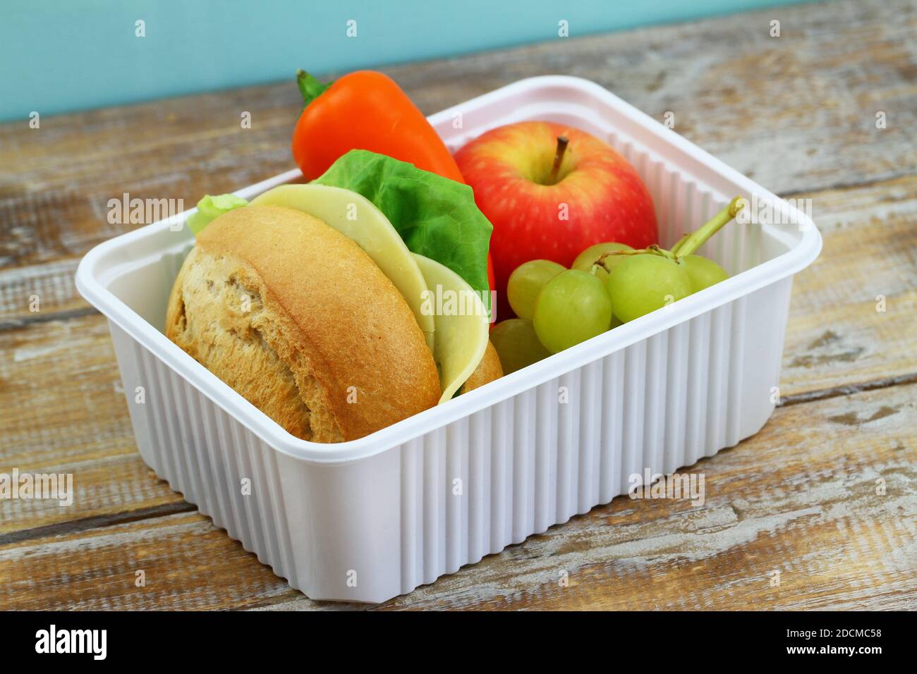 Scatola di pranzo nutriente confezionata contenente sandwich di formaggio marrone, pepe giallo croccante e frutta fresca in scatola di plastica bianca Foto Stock