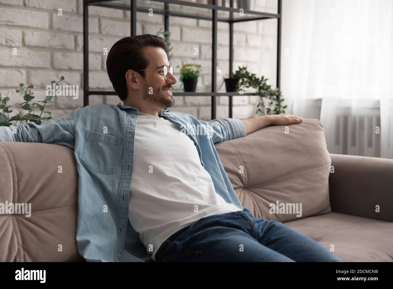 Sorridente giovane bell'uomo in occhiali che si rilassa su un comodo divano. Foto Stock
