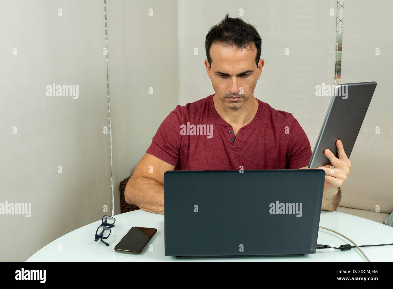 uomo di 44 anni che lavora a casa con computer e tablet (foto 1). Foto Stock