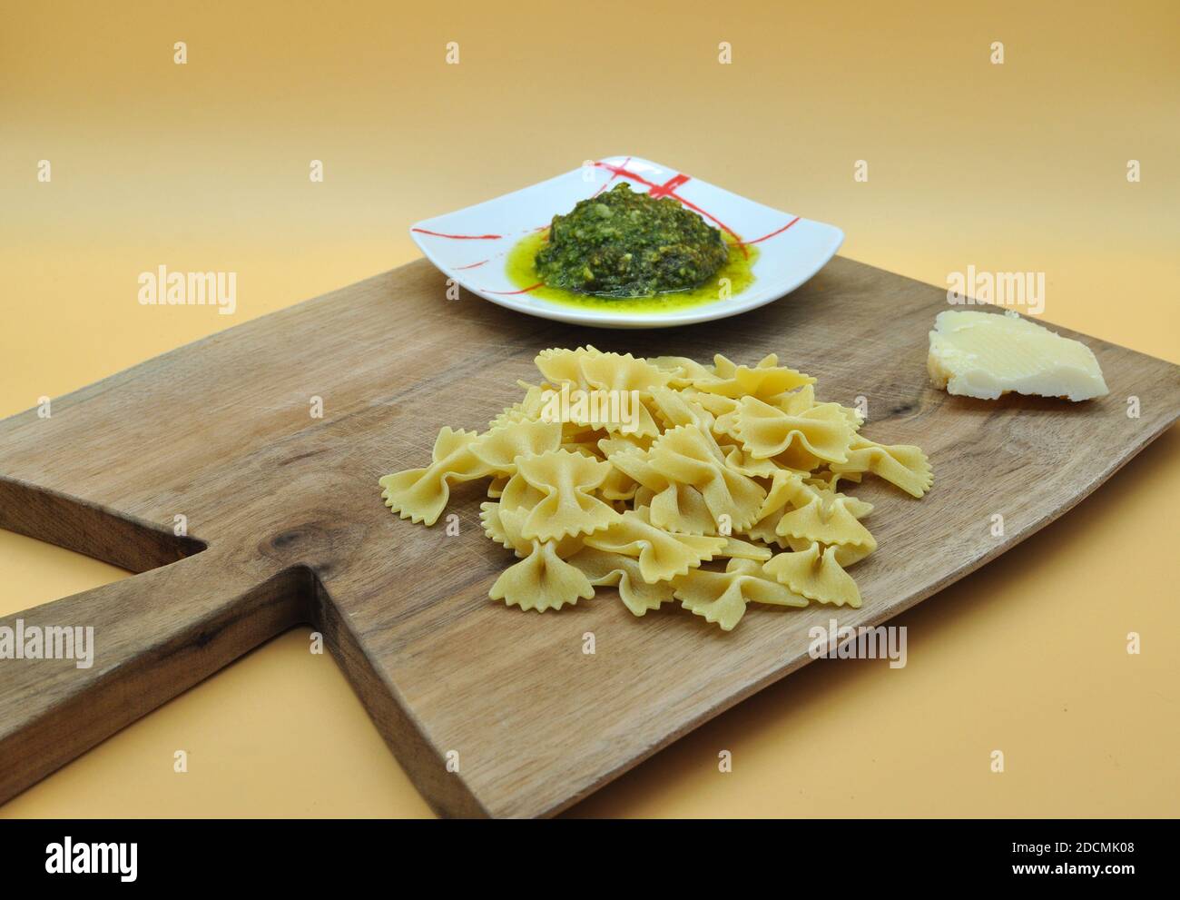Tutto ciò di cui avete bisogno pronto a cucinare un appetitoso farfalle di pasta con pesto genovese con la ricetta italiana perfetta, il tutto posto su un elegante tagliere Foto Stock