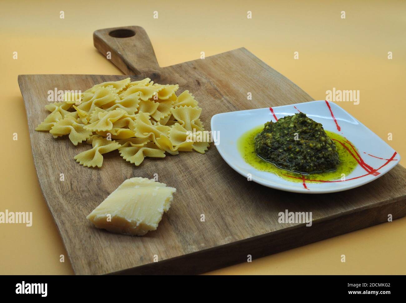 Tutto ciò di cui avete bisogno pronto a cucinare un appetitoso farfalle di pasta con pesto genovese con la ricetta italiana perfetta, il tutto posto su un elegante tagliere Foto Stock