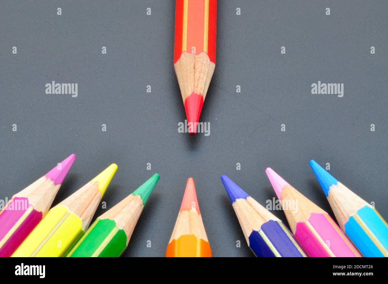 Metafora bullonata con matite colorate che puntano al rosso sopra sfondo nero Foto Stock