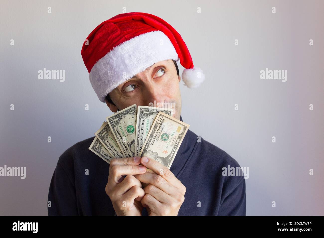 Giovane uomo con cappello di Santa che tiene le fatture del dollaro con  sguardo sognante sopra lo sfondo bianco. Persona che cerca in su con i  contanti nelle mani. Risoluzione del nuovo