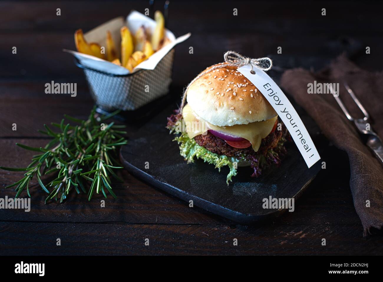 Hamburger di formaggio vegetariano fatti in casa e patatine fritte al buio tavola di legno su un tavolo di legno marrone scuro accanto a. Un tovagliolo di lino marrone con un segno godere Foto Stock