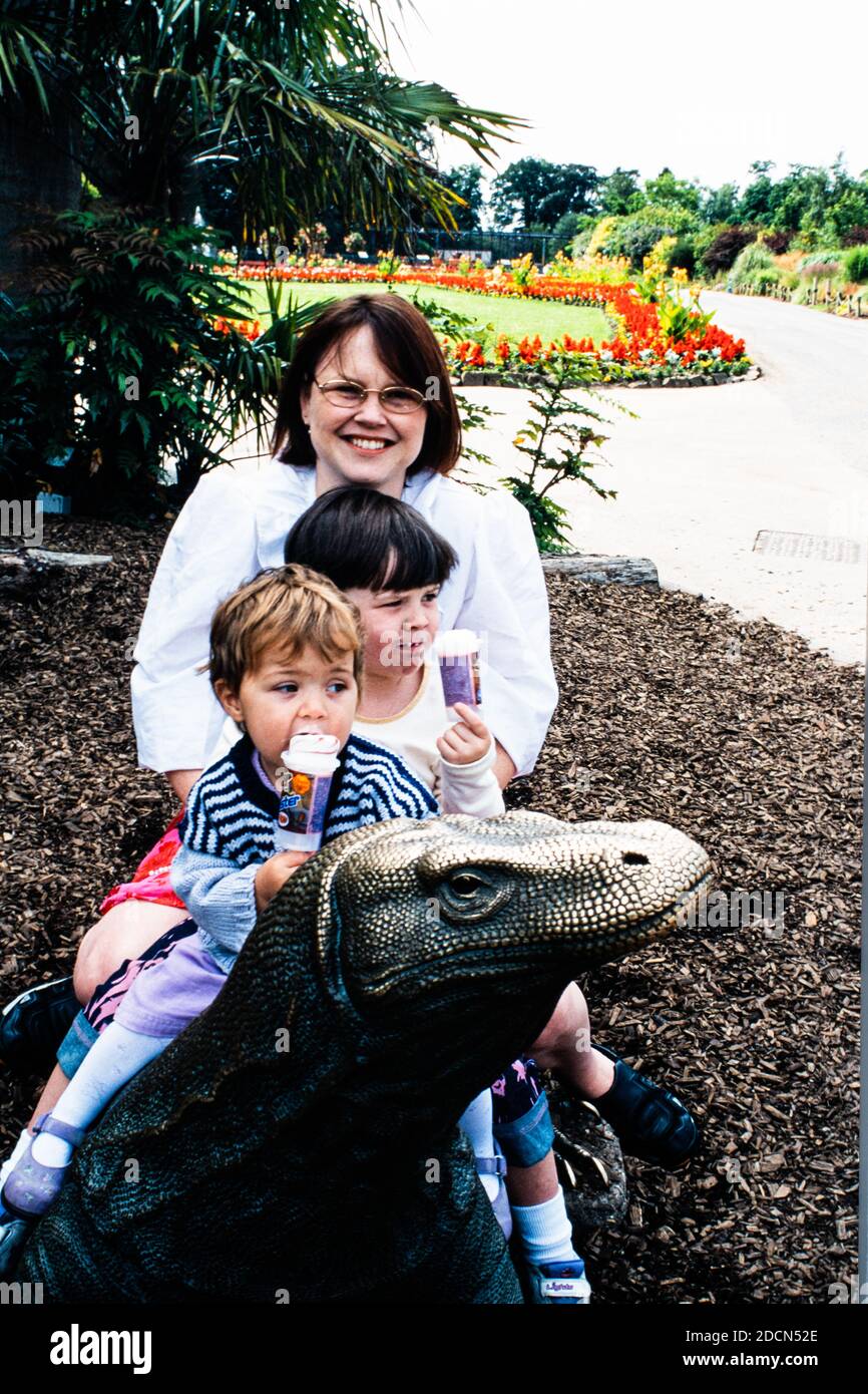 Una famiglia, una donna e due ragazze, seduti su una scultura in bronzo del drago Comodo allo zoo di Chester, Regno Unito Foto Stock
