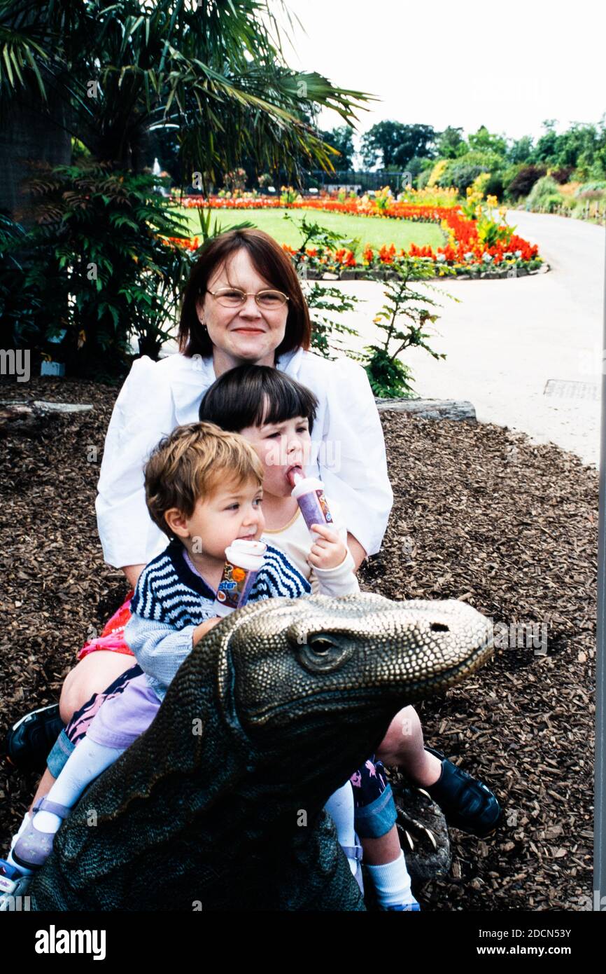 Una famiglia, una donna e due ragazze, seduti su una scultura in bronzo del drago Comodo allo zoo di Chester, Regno Unito Foto Stock
