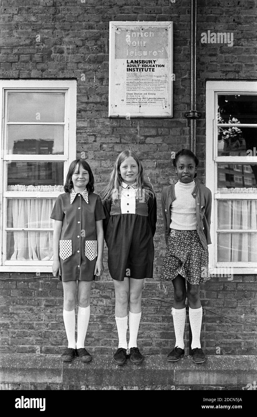 Regno Unito, Londra, Docklands, Isle of Dogs, 1974, Cubitt Town, Glengall Grove Primary School (background). Segno che promuove l'istituto di formazione dell'adulto di Lansbury dietro gli allievi. La scuola è ancora lì: Cubitt Town Infant & Junior School. Foto Stock