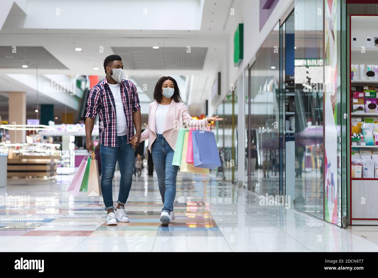 Giovane coppia nera che indossa una maschera medica protettiva che cammina dentro centro commerciale Foto Stock