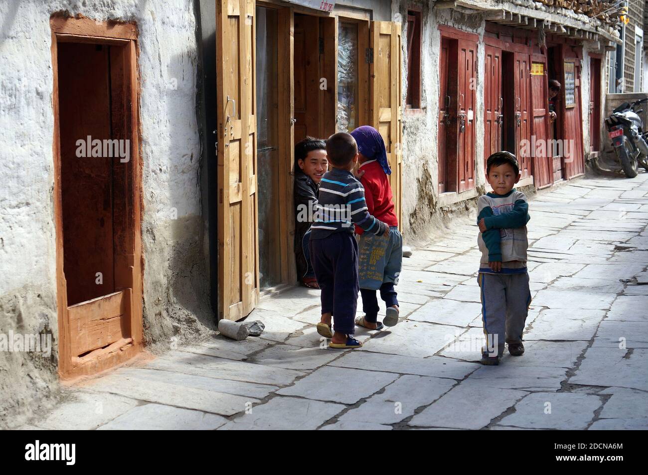 I bambini di etnia tibetana giocano sul marciapiede acciottolato di una strada cittadina in una giornata di sole. Foto Stock