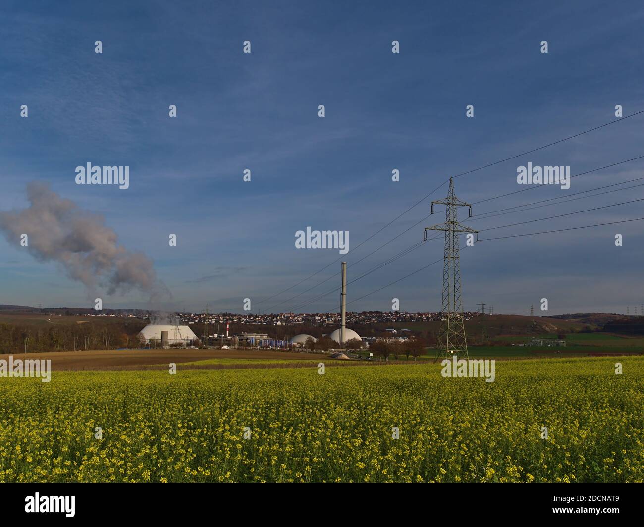 Centrale nucleare a Neckarwestheim, Germania, situata sulla riva del fiume Neckar, con linea elettrica, pilone e un fiorente campo agricolo. Foto Stock