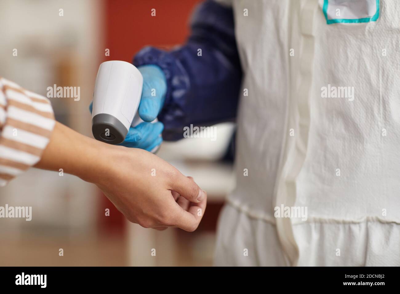 Primo piano di un operatore medico irriconoscibile che controlla la temperatura con un termometro senza contatto rivolto verso le mani femminili, spazio di copia Foto Stock