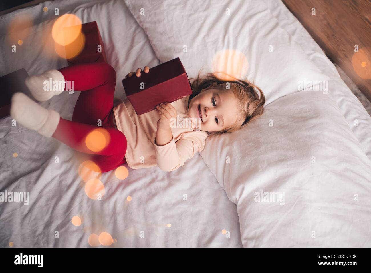 Divertente bambina di 2-3 anni con pigiami sdraiati a letto con scatola regalo di Natale e luce incandescente. Felicità. Vista dall'alto. Infanzia. Foto Stock
