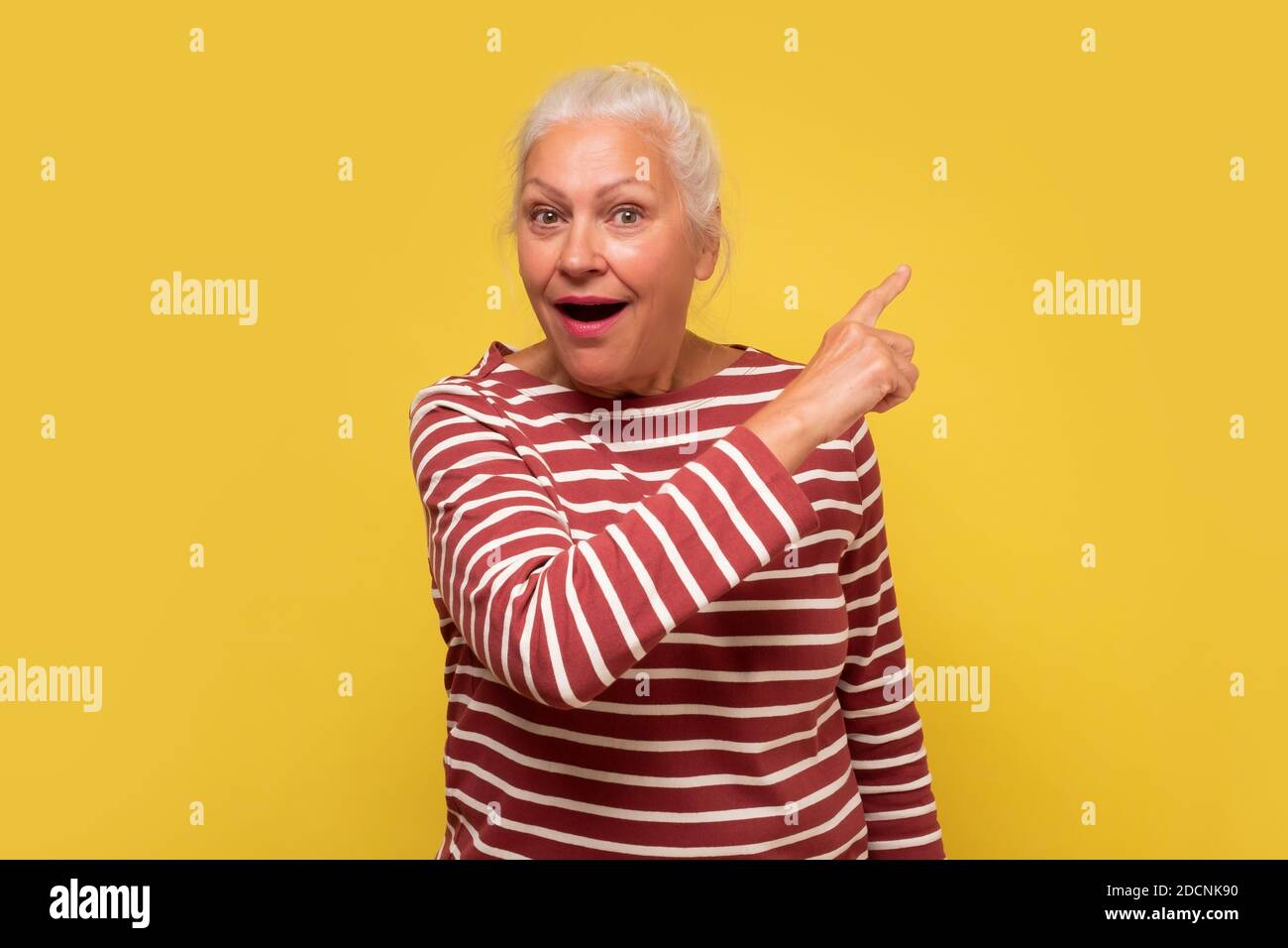 Stupito vecchia donna che indica lo spazio di copia da parte, guardando la macchina fotografica che fa pubblicità al servizio di prodotto o l'offerta di prezzo poco costosa. Scatto in studio. Foto Stock