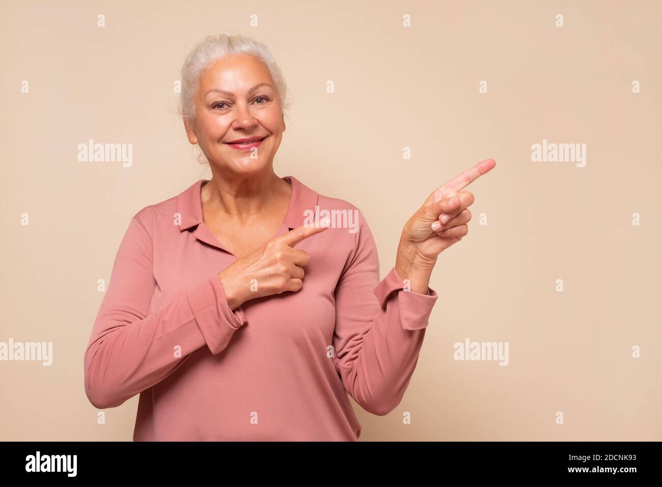 Stupito vecchia donna che indica lo spazio di copia da parte, guardando la macchina fotografica che fa pubblicità al servizio di prodotto o l'offerta di prezzo poco costosa. Scatto in studio. Foto Stock