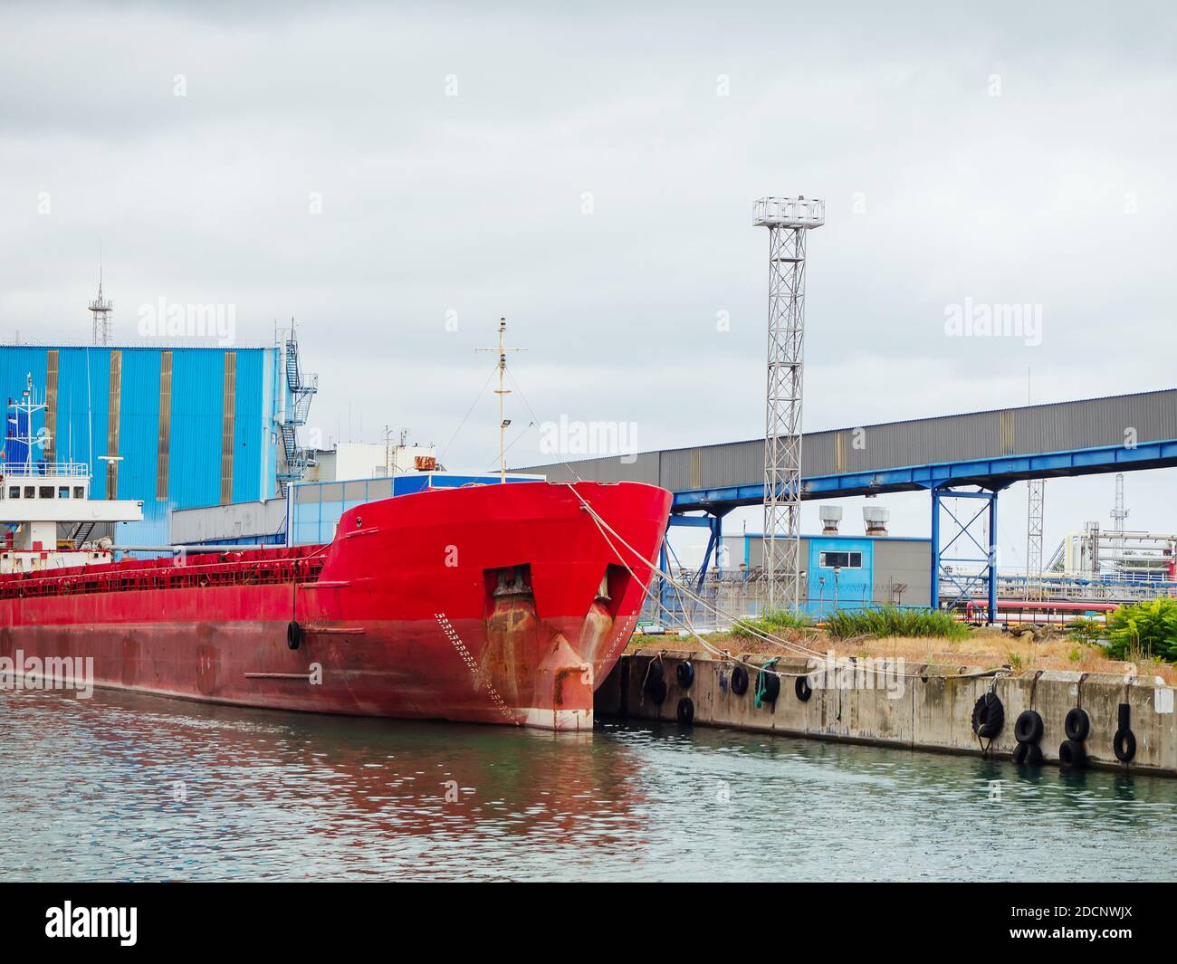 Grande imbarcazione industriale rossa ormeggiata al molo con blu strutture con rifilatura metallica Foto Stock