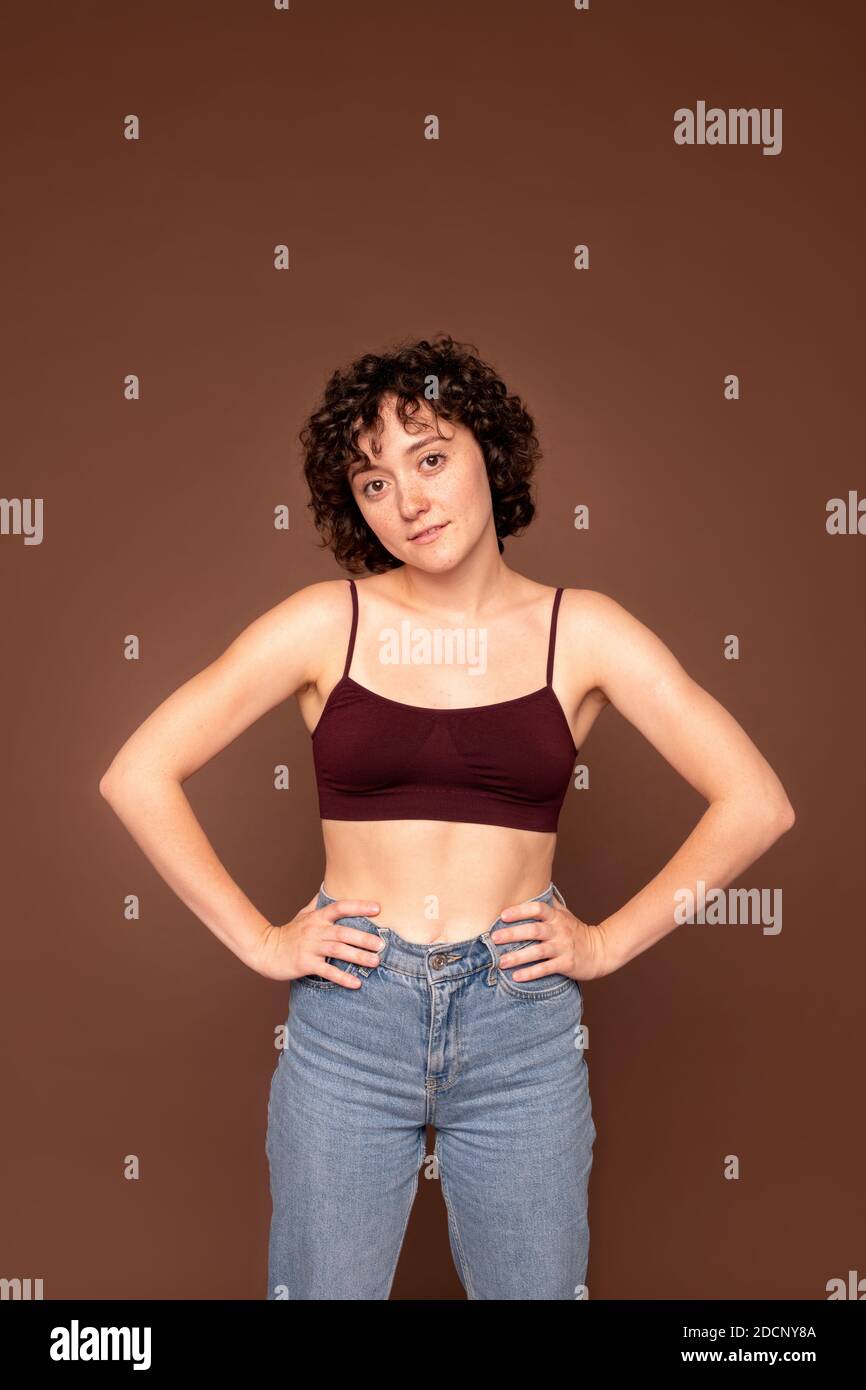 Giovane donna bruna bellissima con capelli ricci corti che la tengono mani sulla vita Foto Stock