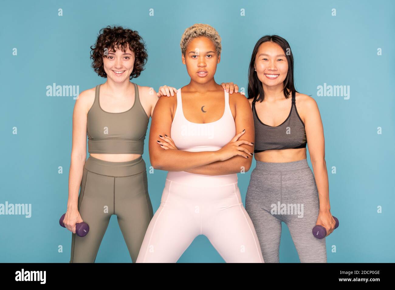 Due sportive felici con manubri in piedi dalla loro femmina di razza mista amico Foto Stock