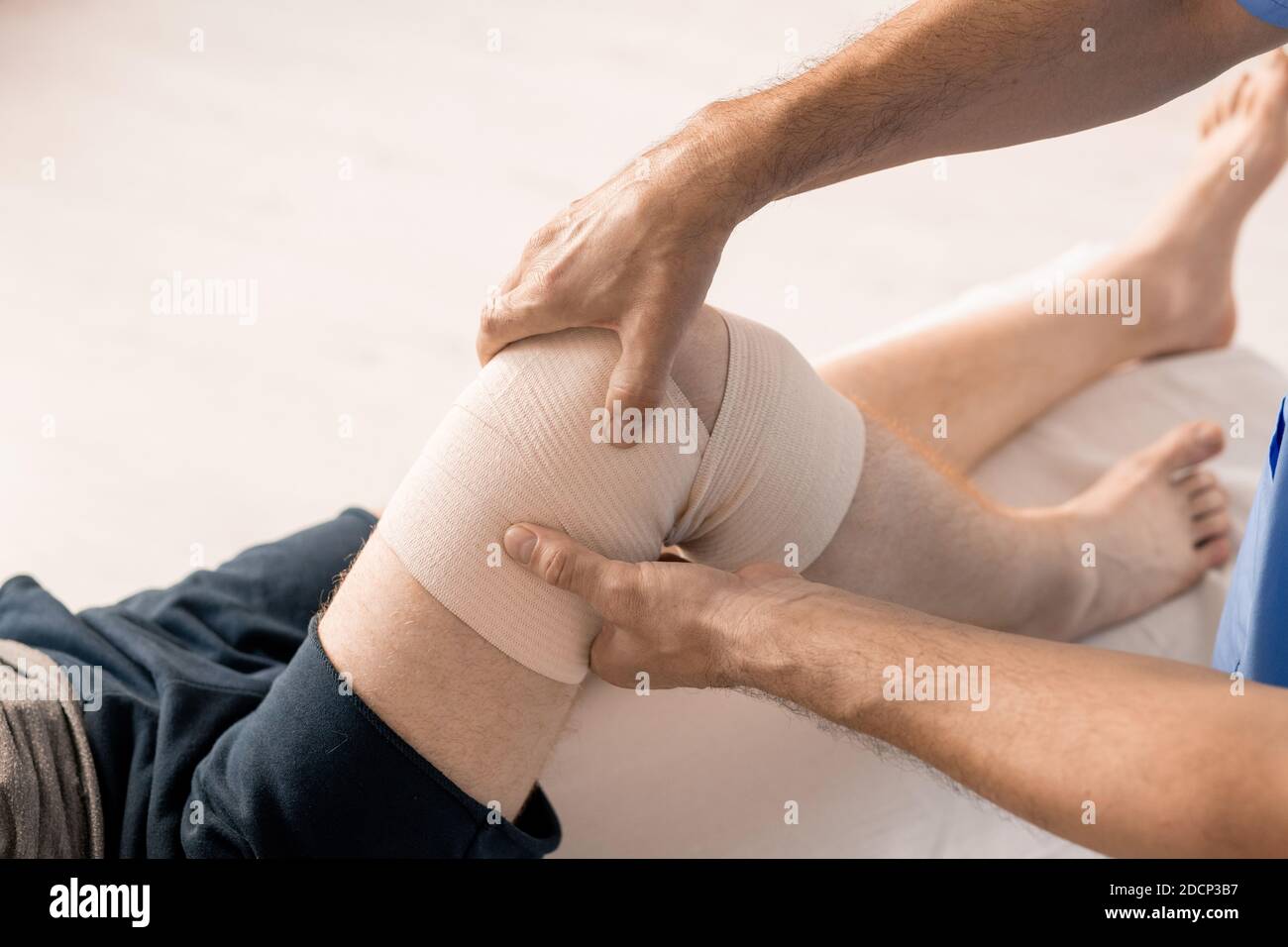 Mani di un medico di sesso maschile che avvolge il ginocchio del paziente disabile con bendaggio flessibile Foto Stock