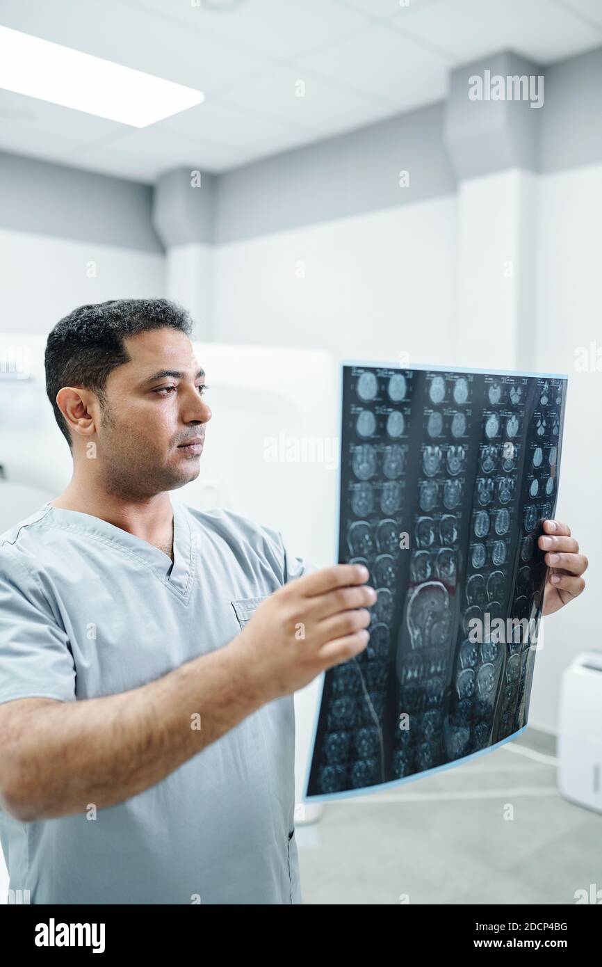 Radiologo maschile sicuro in uniforme guardando l'immagine radiografica di uno dei pazienti Foto Stock