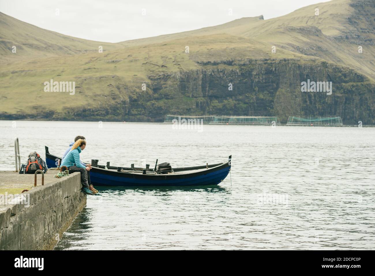 I viaggiatori irriconoscibili si rilassano sul molo di cemento vicino alla barca contro il mare e in collina Foto Stock