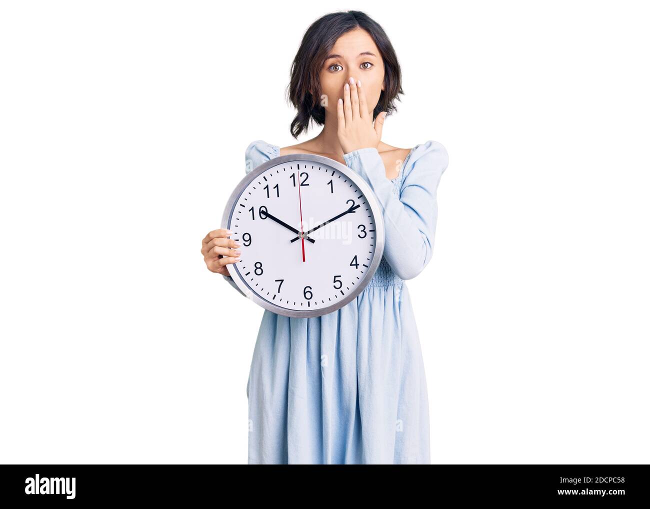 Giovane bella ragazza che tiene grande orologio che copre la bocca con la  mano, scioccata e impaurita per errore. Sorpresa espressione Foto stock -  Alamy