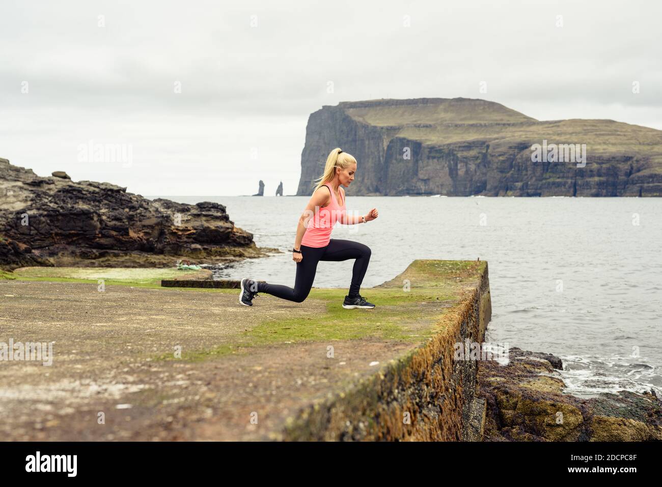 Atleta femminile che si affondo sulla costa mussosa vicino al mare durante il fitness allenamento in natura Foto Stock