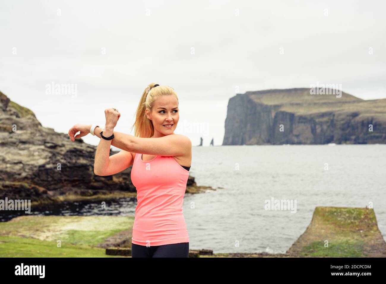 Atleta femminile che allunga le braccia e guarda via durante l'allenamento costa vicino al mare Foto Stock