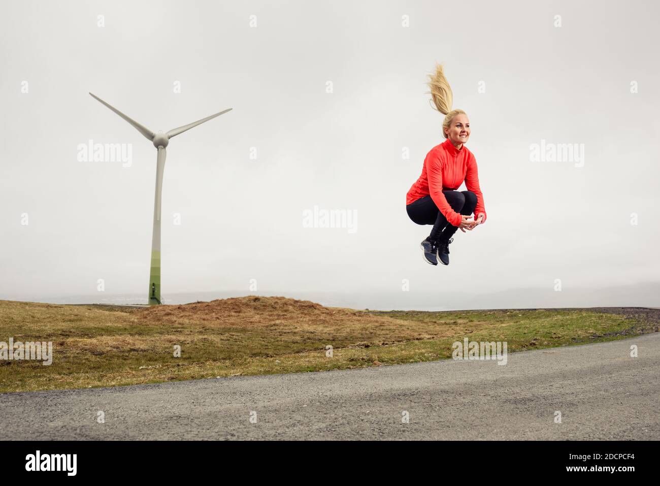 Felice atleta che salgono su strada asfaltata vicino al mulino a vento durante l'allenamento in natura Foto Stock