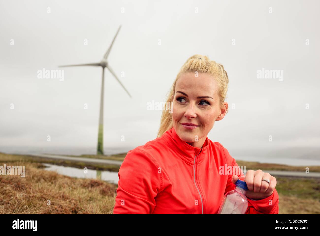 Atleta adulta che apre una bottiglia d'acqua durante l'allenamento vicino mulino a vento Foto Stock