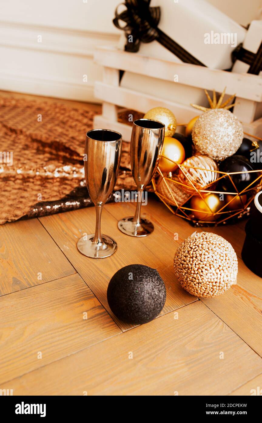 Due bicchieri in metallo oro da bere su pavimento in legno con decorazioni per Natale in tonalità oro e nero: Palline rotonde lucide, scatole regalo, ghirlande e cenere Foto Stock