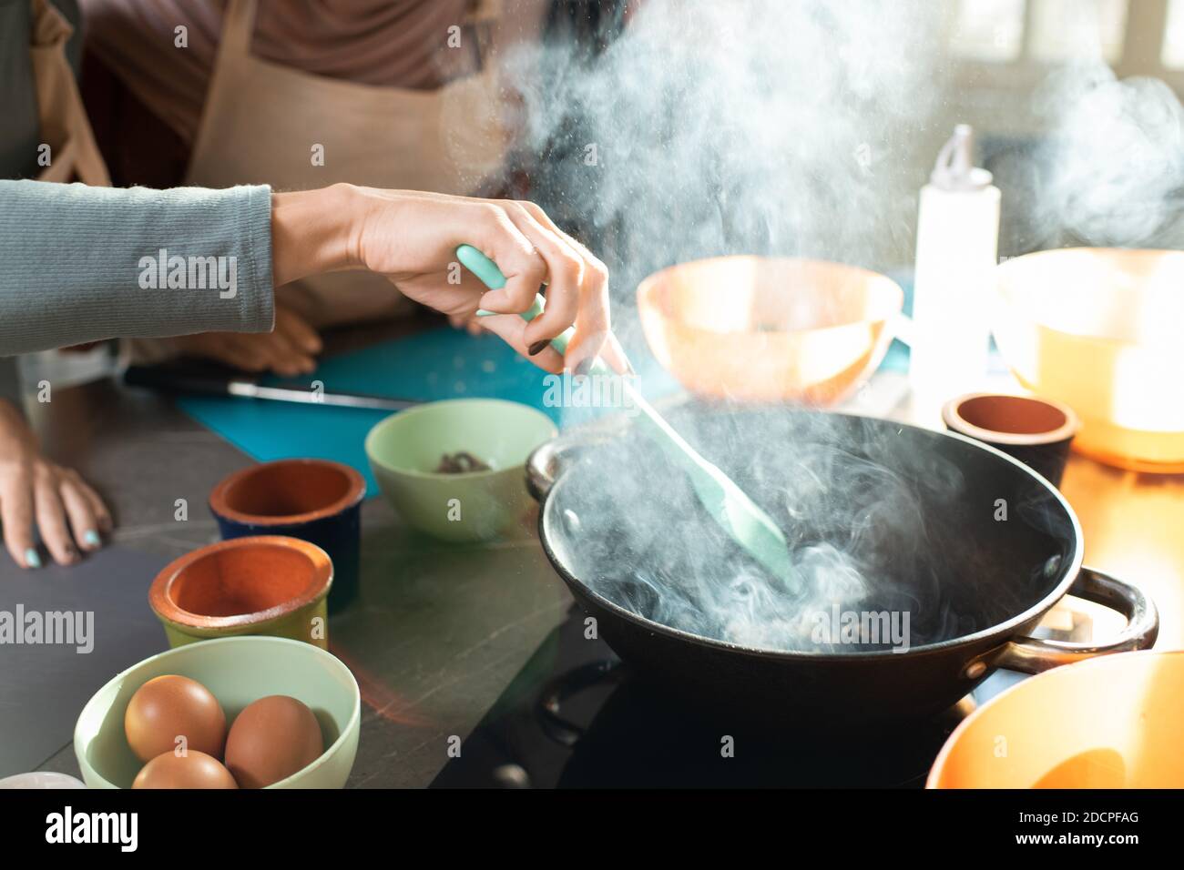 Mano di giovane donna con spatola termoresistente che mescola gli ingredienti in padella Foto Stock