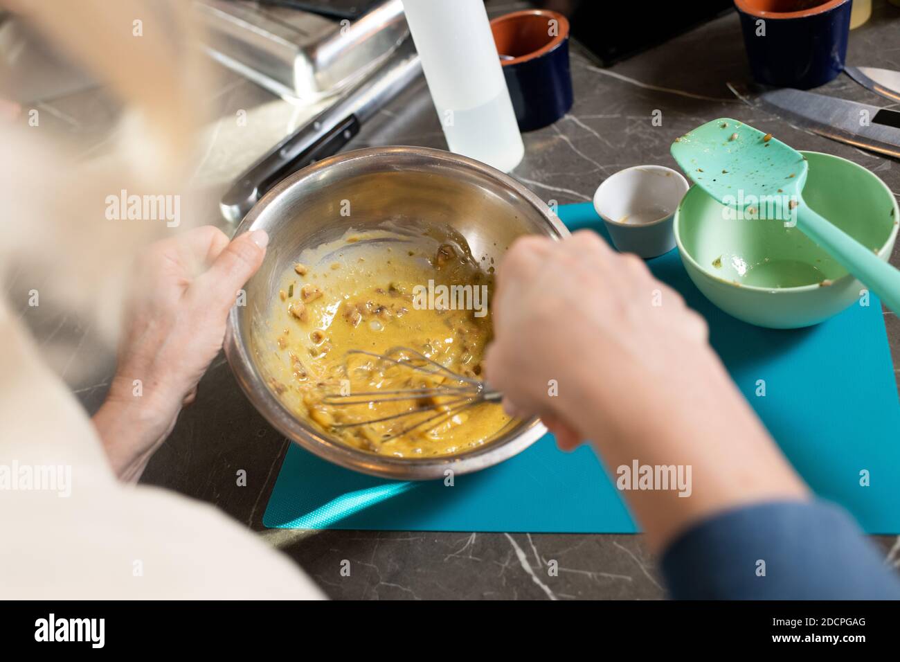 Mani di donne mature mescolando ingredienti con whisker in metallo ciotola per tavolo Foto Stock