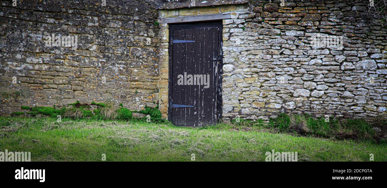 Un muro di pietra medievale coperto da lichene ha un misterioso vibe con una porta di legno invecchiata che porta a qualche luogo sconosciuto In Inghilterra rurale Foto Stock