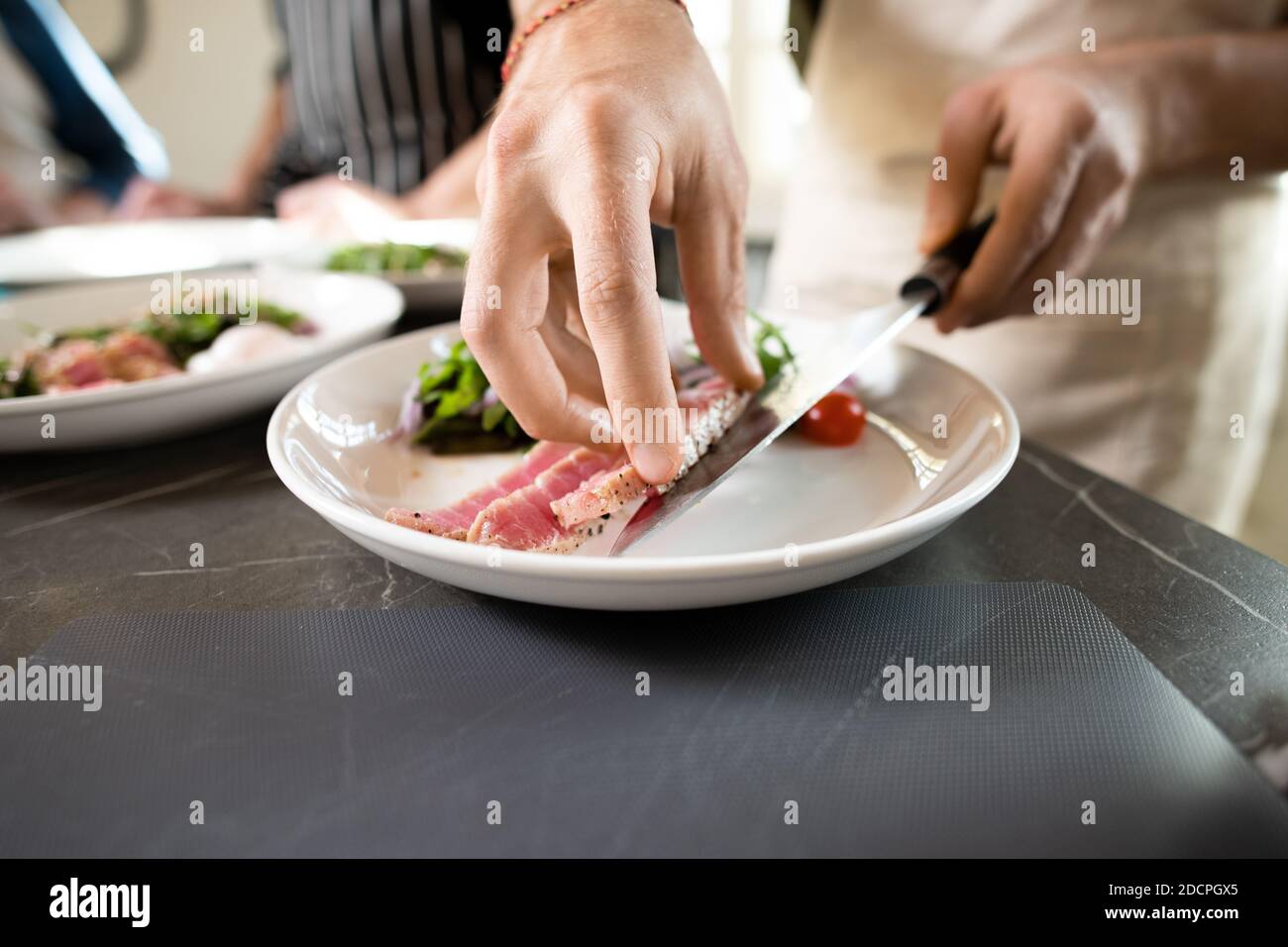 Mani di giovane maschio in grembiule mettendo pezzo di affumicato o manzo alla griglia su piatto Foto Stock