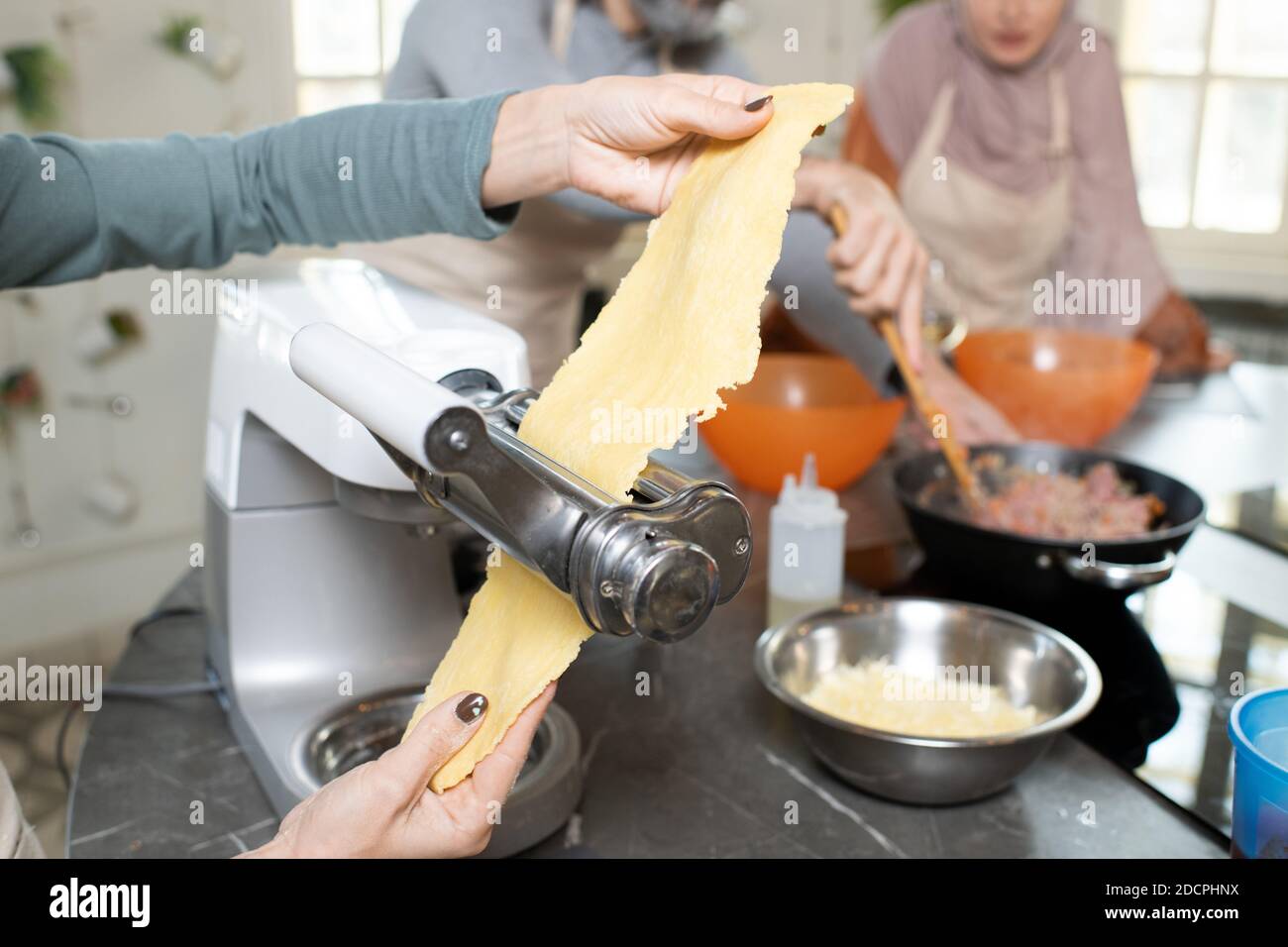 Mani di giovane donna che tengono pezzo di pasta arrotolata mentre utilizzo di un dispositivo da cucina Foto Stock