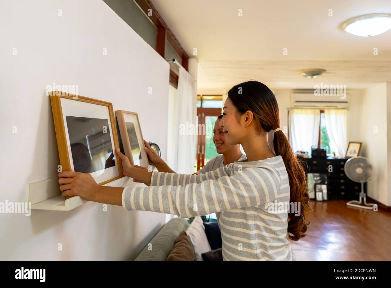Giovane coppia appeso cornice foto sulla parete nella loro nuova casa. Sorridente marito e moglie felice di stabilirsi insieme in casa di proprietà di recente Foto Stock