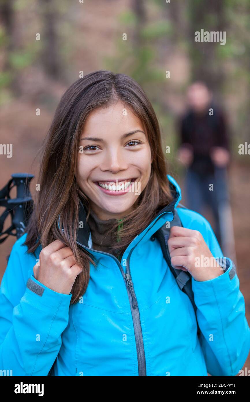 Felice ragazza escursionista asiatica in foresta con zaino e bastoni da trekking a piedi con il gruppo di amici. Sano sorriso turista cinese donna. Foto Stock