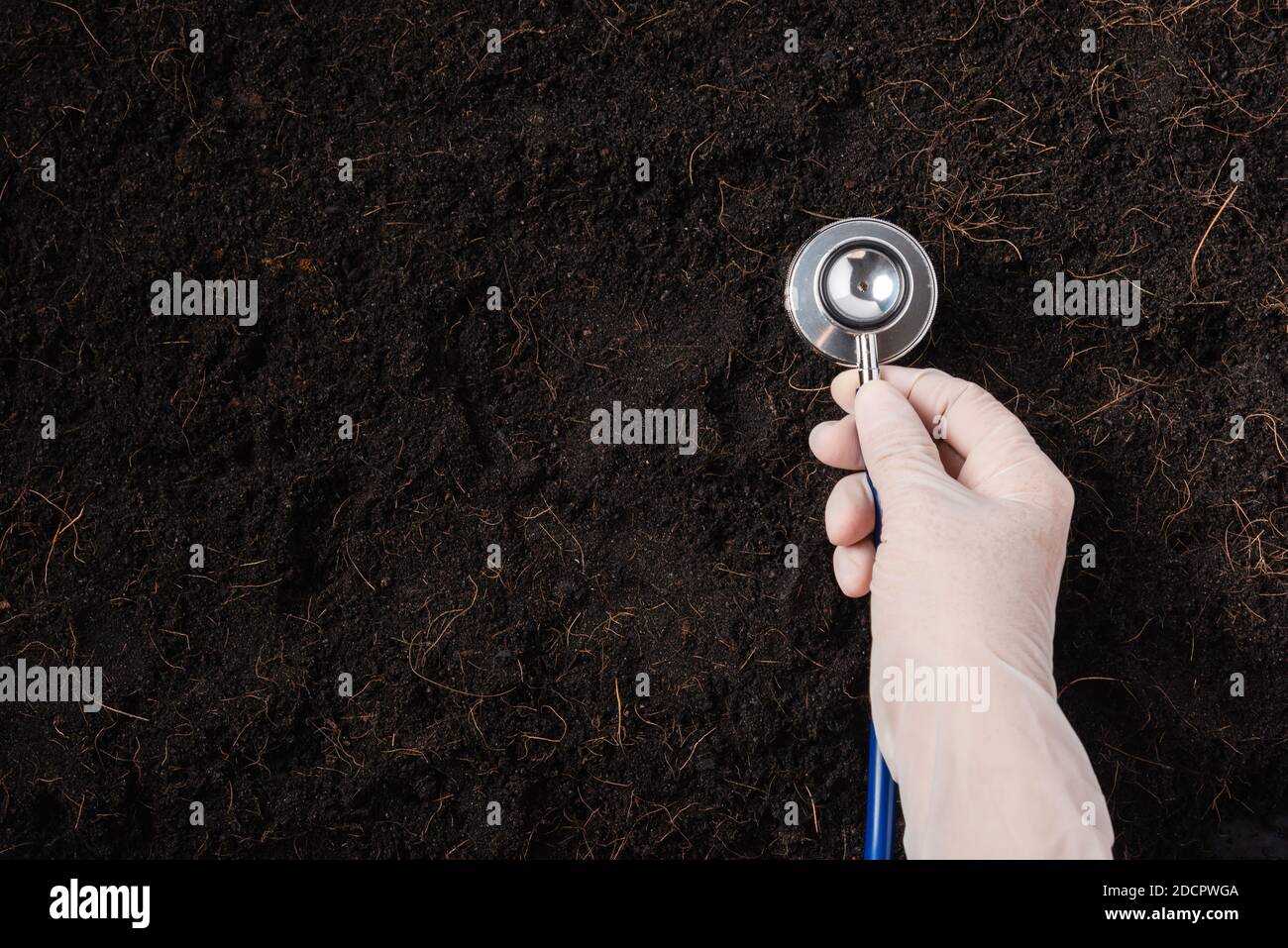 Mano di donna ricercatrice indossare guanti che tengono uno stetoscopio su terreno fertile nero per controllare la condizione prima di agricoltura o piantare, concetto di mondo Foto Stock