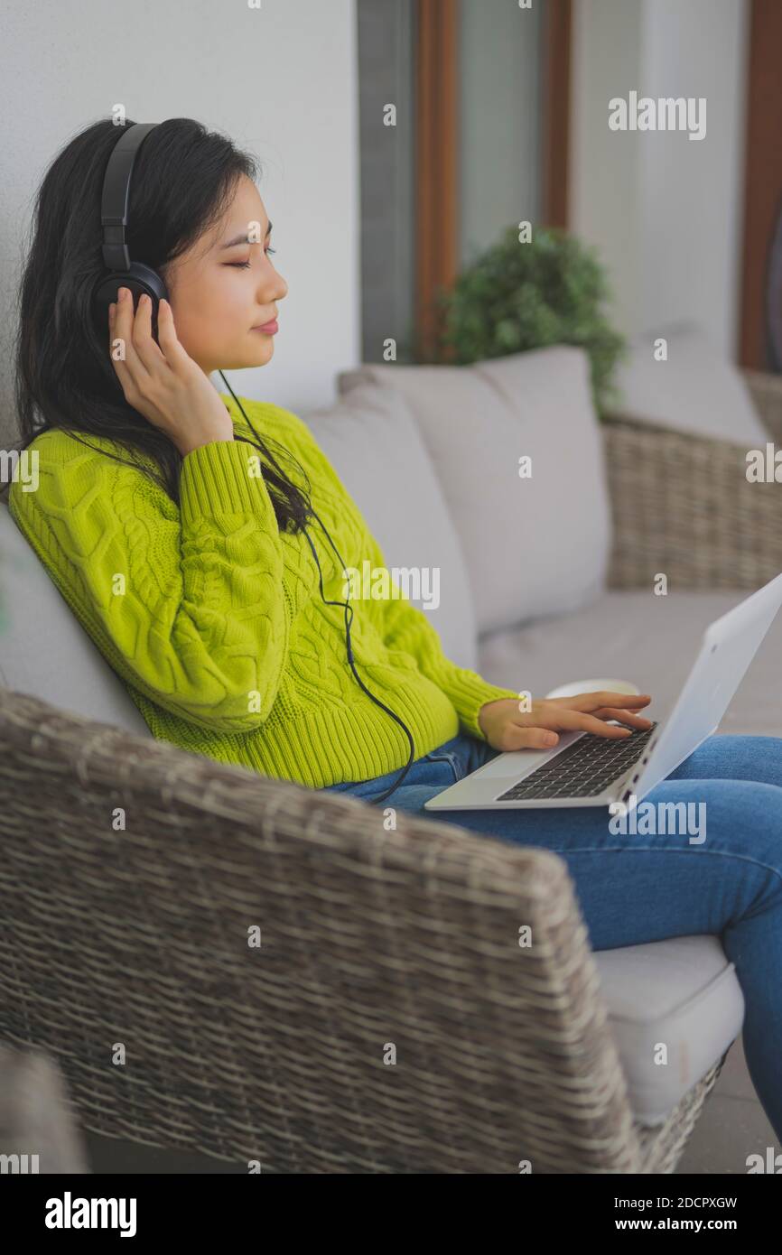 Giovane donna asiatica che ascolta la musica dal computer portatile utilizzando le cuffie. Freelancng o concetto di apprendimento a distanza. Foto di alta qualità Foto Stock