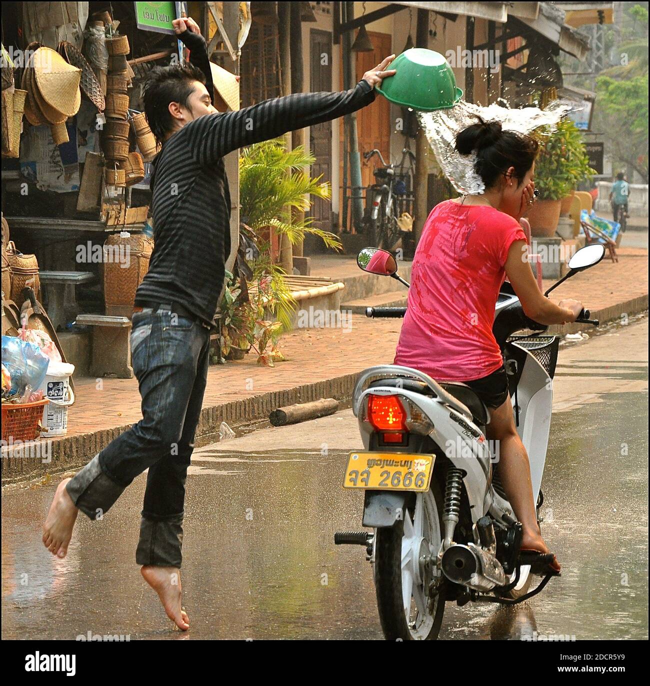 Giovane uomo che getta l'acqua su un motociclista che passa durante il Songkran Water Thringing Festival. Foto Stock