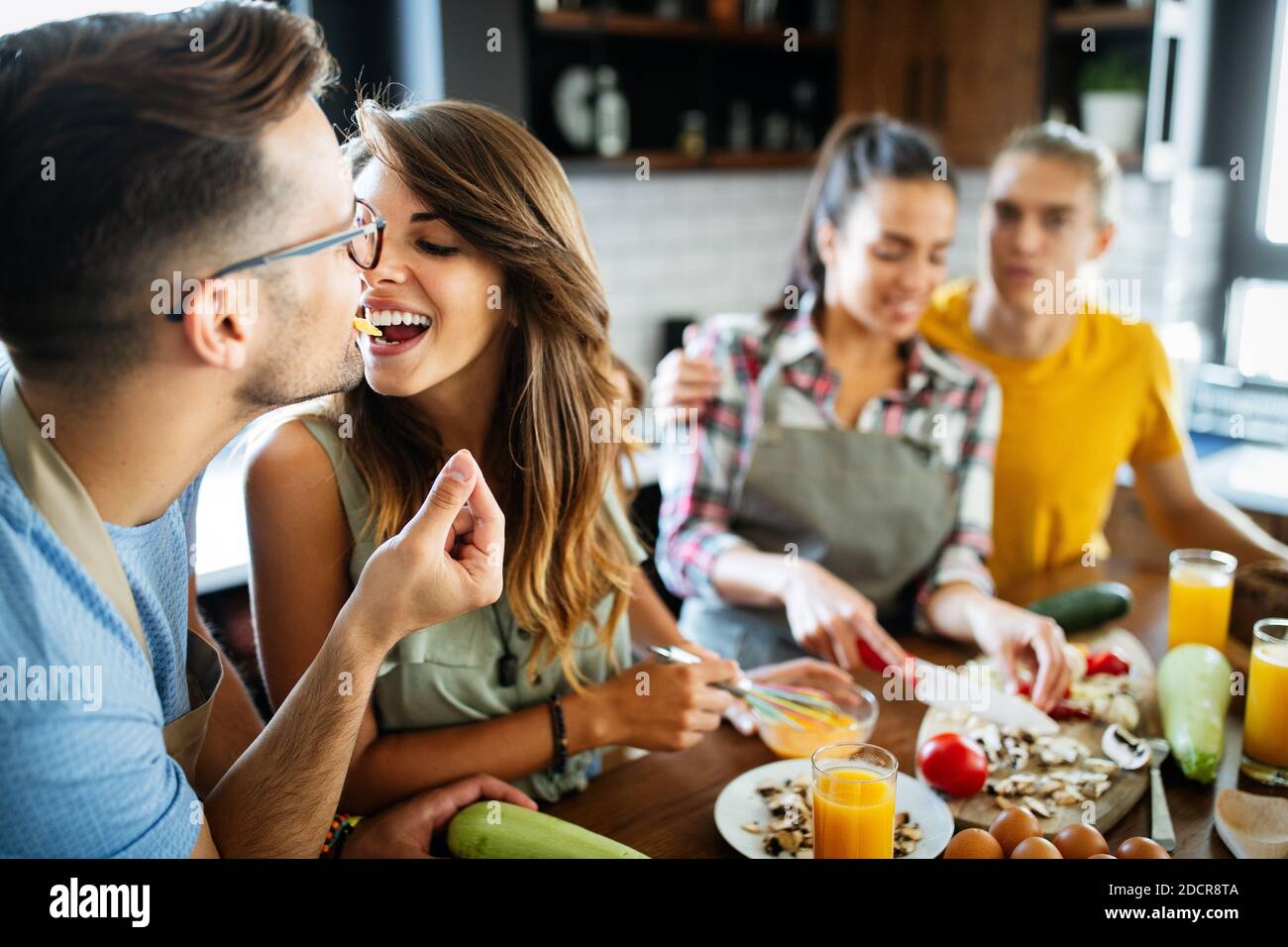 Gruppo di amici felici che ridono e parlano mentre preparano i pasti in cucina Foto Stock