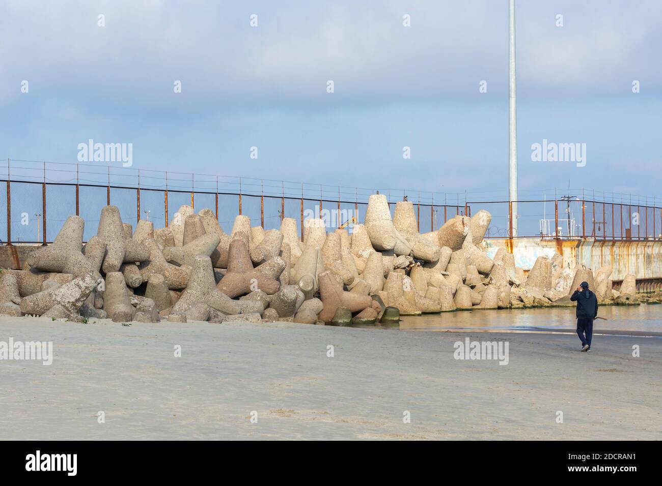 Un gruppo di grandi frangiflutti in cemento si trovano sulla riva vicino al molo. Foto Stock